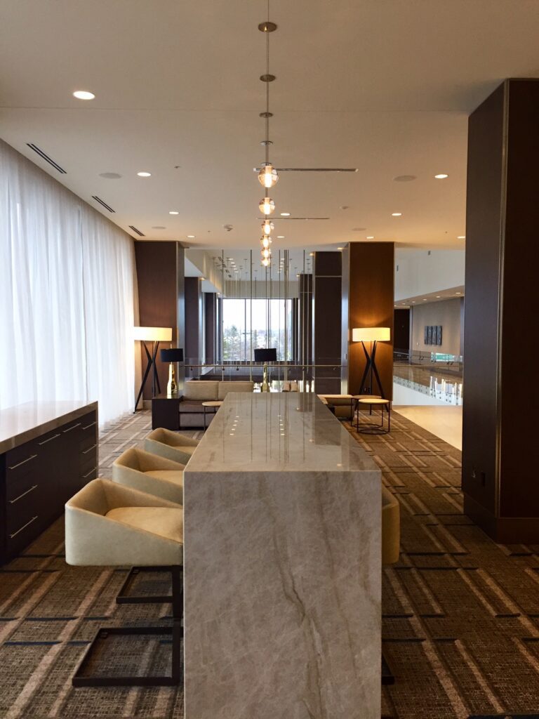 Lounge working area. Contains patterned carget, a granite desktop with lined chairs, and overhead hanging lighting.