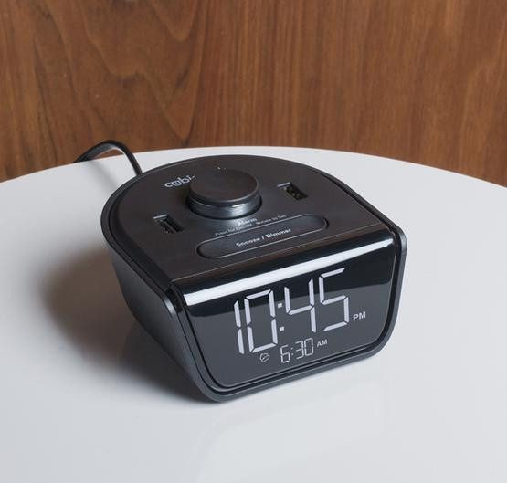A small black alarm clock sitting on a bed side table