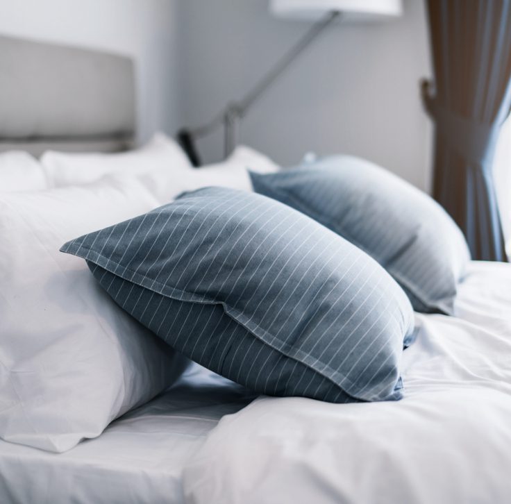 close up of a bed with white bedding and blue accent pillow with stripes