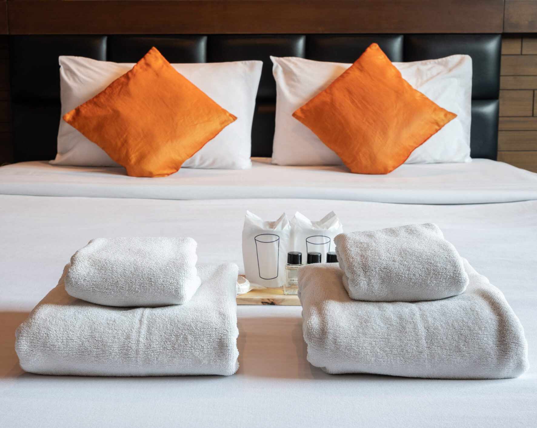 Hotel bed with orange decorative pillows and towels at the end of the bed