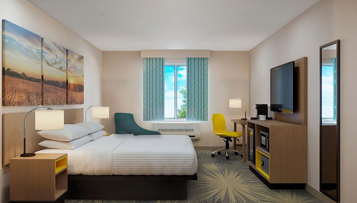 Hotel room with one king size bed, small desk with a yellow chair and a tv