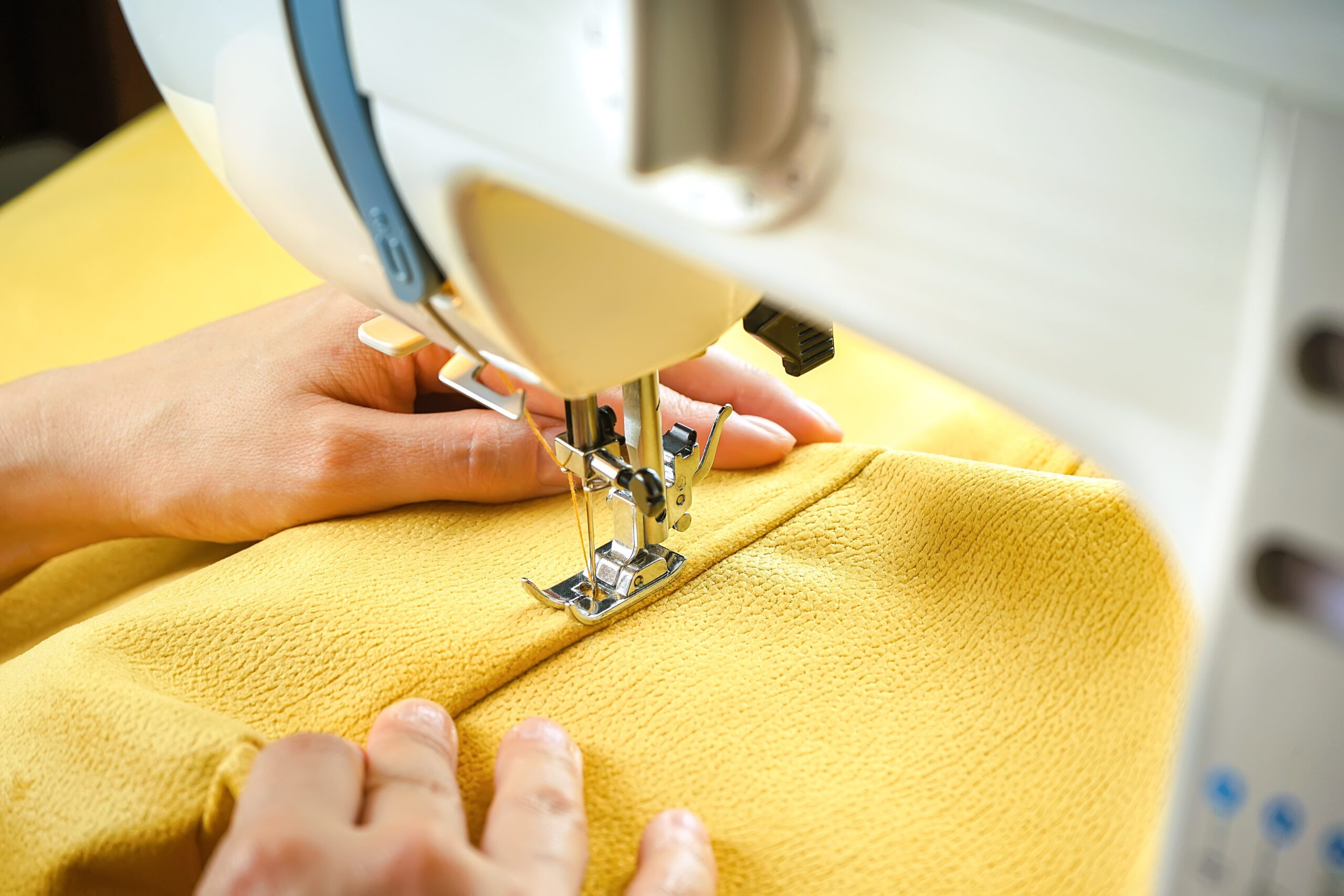 Pair of hands stitching yellow fabric togther with a modern sewing machine.