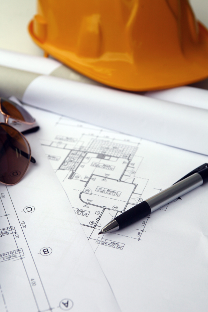 Pen, sunglasses, and an orange hardhat sitting on top of a set of blueprints.